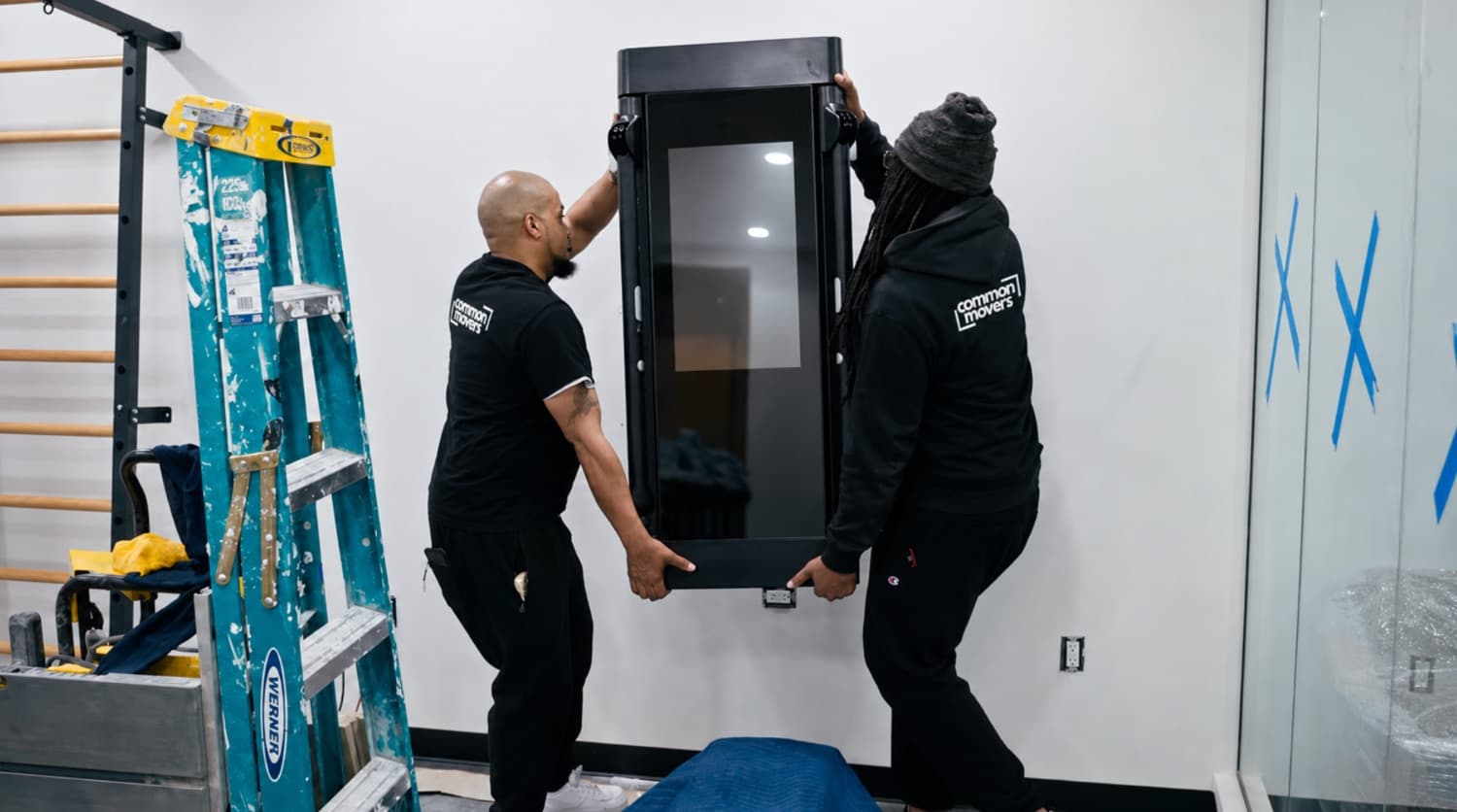 A Common Movers crew carrying a treadmill into a home gym